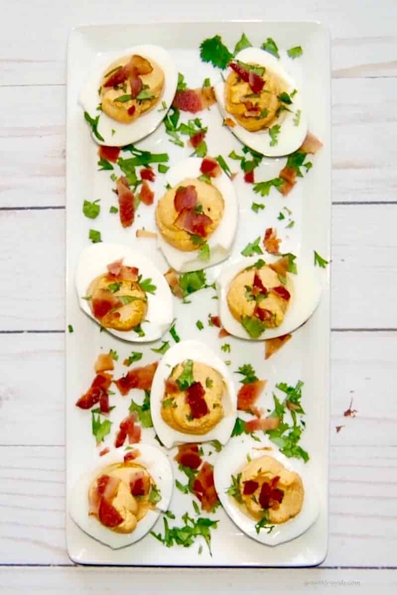 Overhead shot of deviled eggs on a platter sprinkled with bacon and parsley.