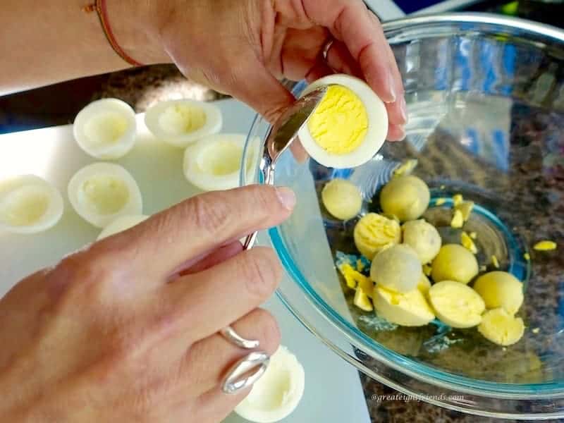 Hands removing the yolk from hard boiled eggs with a spoon.