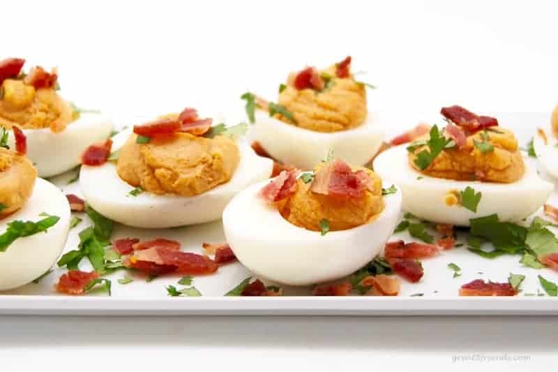 Deviled eggs on a platter sprinkled with bacon and parsley.