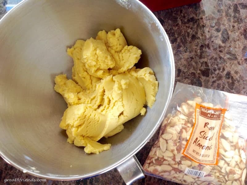 A bowl of dough with a bag of sliced almonds next to it.