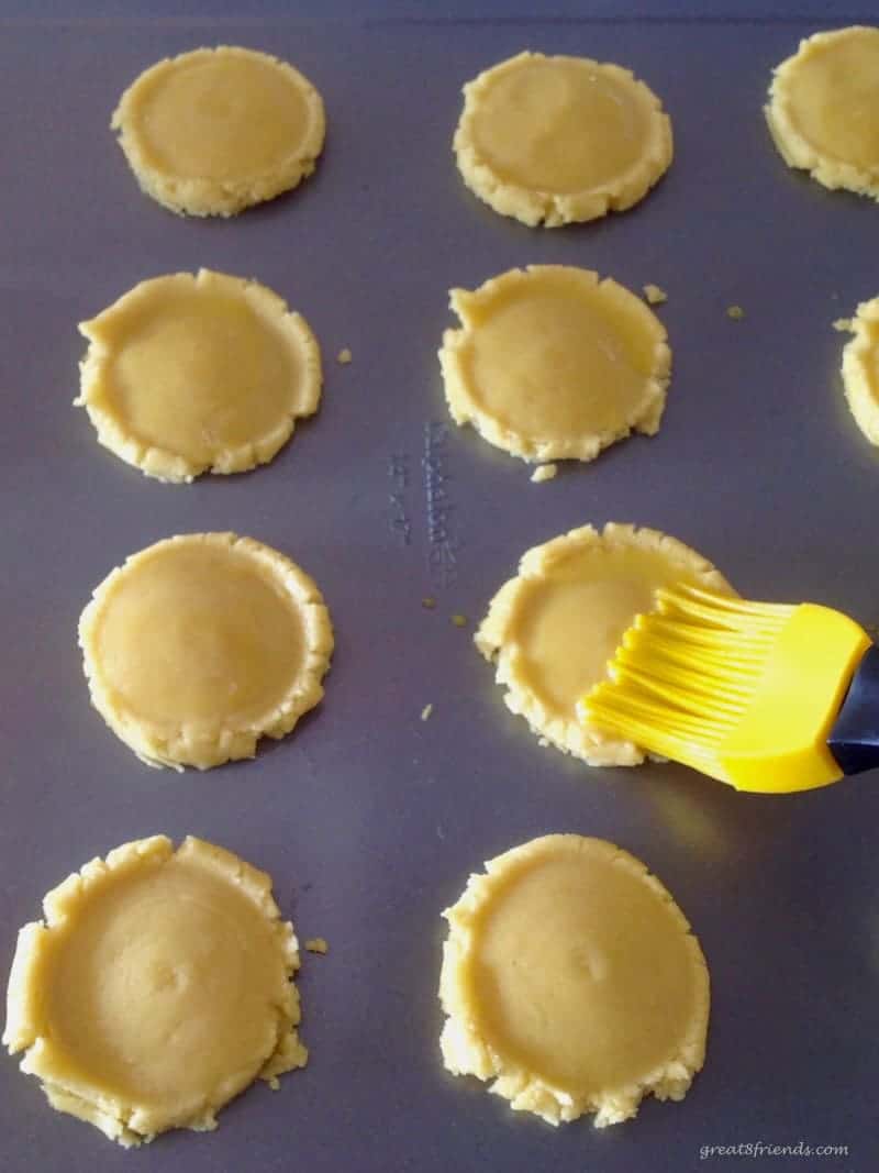 Flattened unbaked cookies being brushed with egg wash.