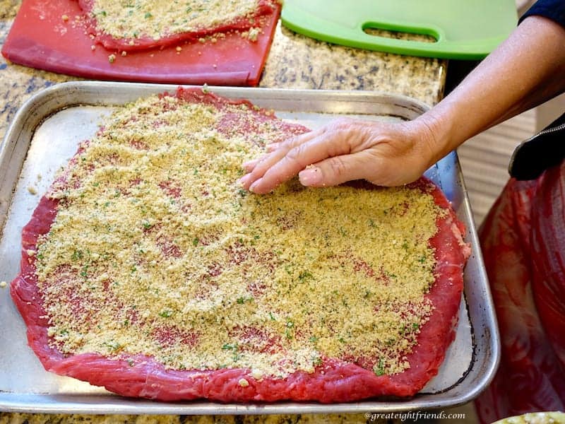 Flank steak laid flat on a baking sheet with bread crumbs spread on top.