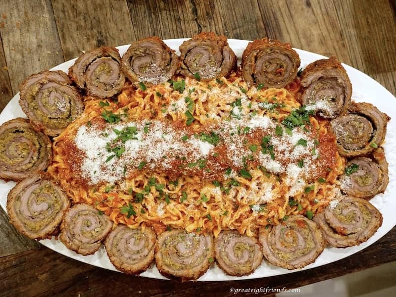 Sliced Beef Braciole Served on a large platter with pasta and rede sauce in the middle. 