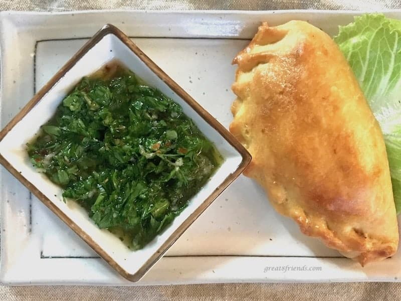 One chorizo empanadas on a small plate with a small side bowl of board dressing.