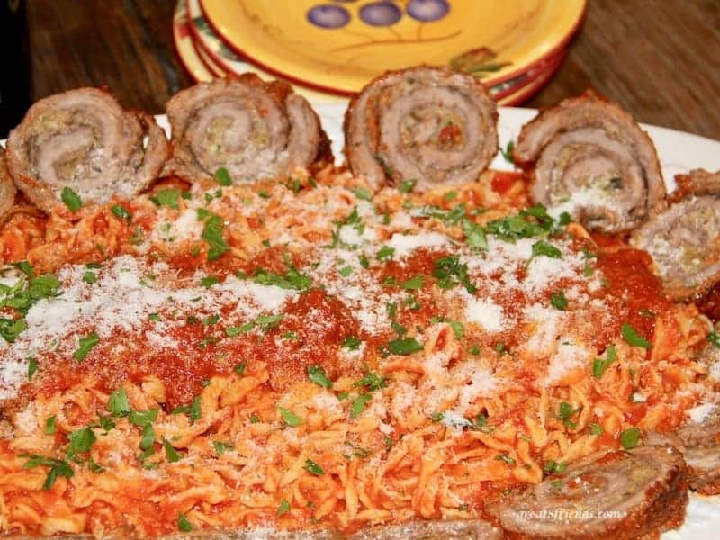 Platter of beef braciole on the rim with spaghetti and pasta sauce in the middle sprinkled with parmesan cheese and parsley.
