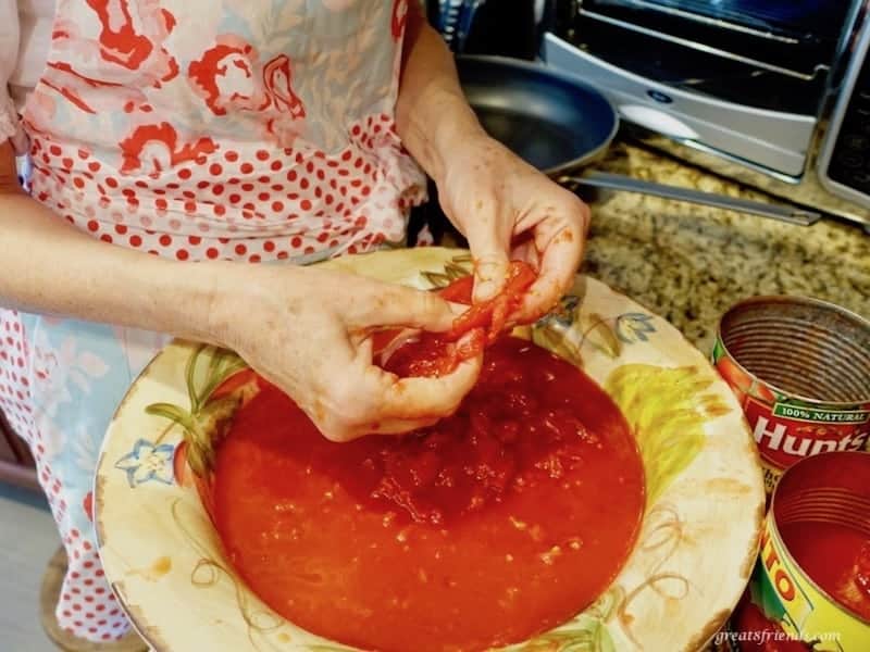 Canned tomatoes being broken apart with a woman's hands.