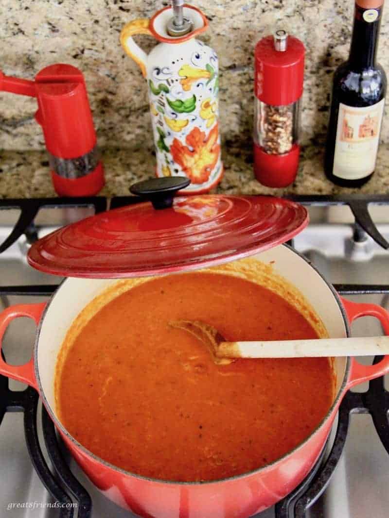 Large red pot on the stove with Italian red sauce in it being stirred with a wooden spoon.