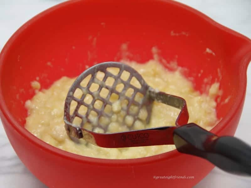 Mashed bananas in a red bowl with the masher in the bowl.
