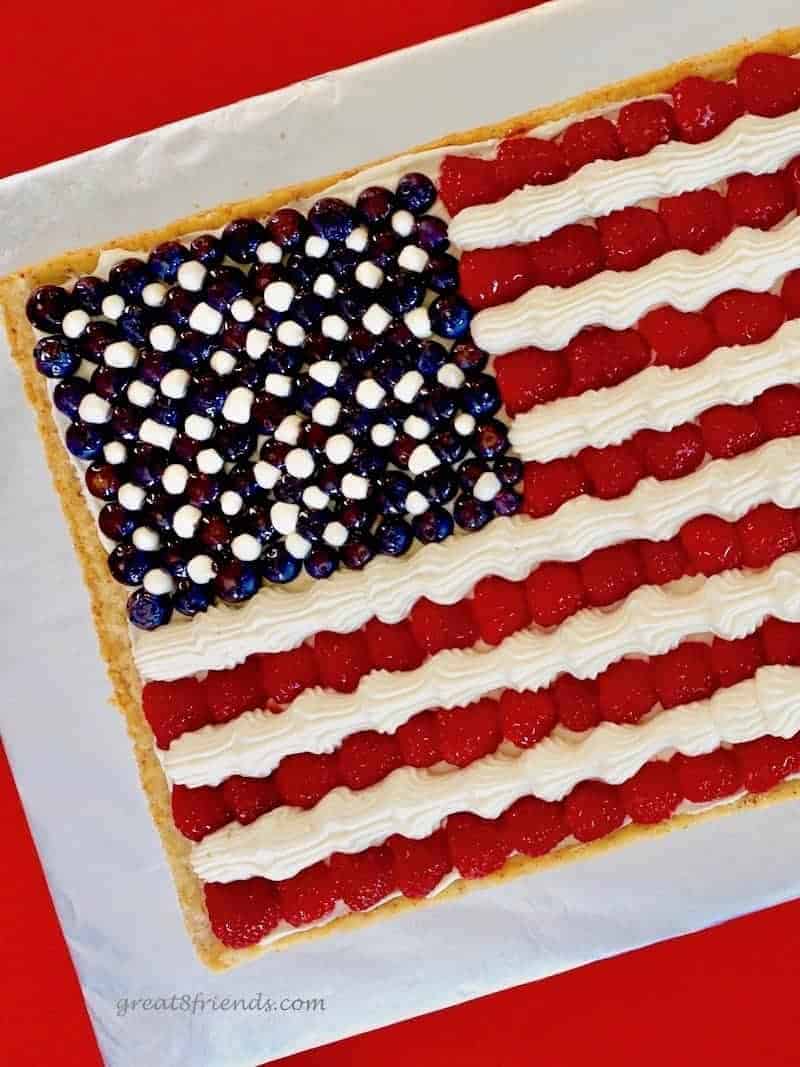 Overhead view of an American Flag Fruit Pizza made with a cookie crust, cheesecake mousse for the stripes and stars and raspberries as the red stripes and blueberries.