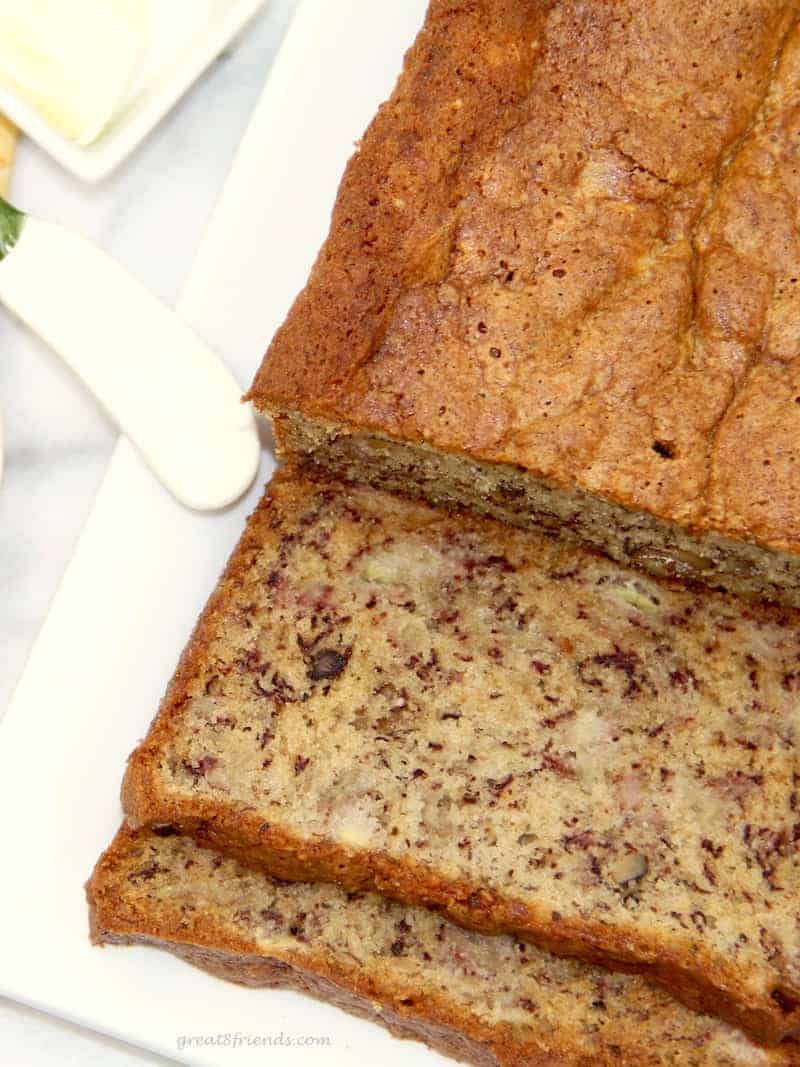 Sliced banana bread on a white plate with butter and butter knife on the side.