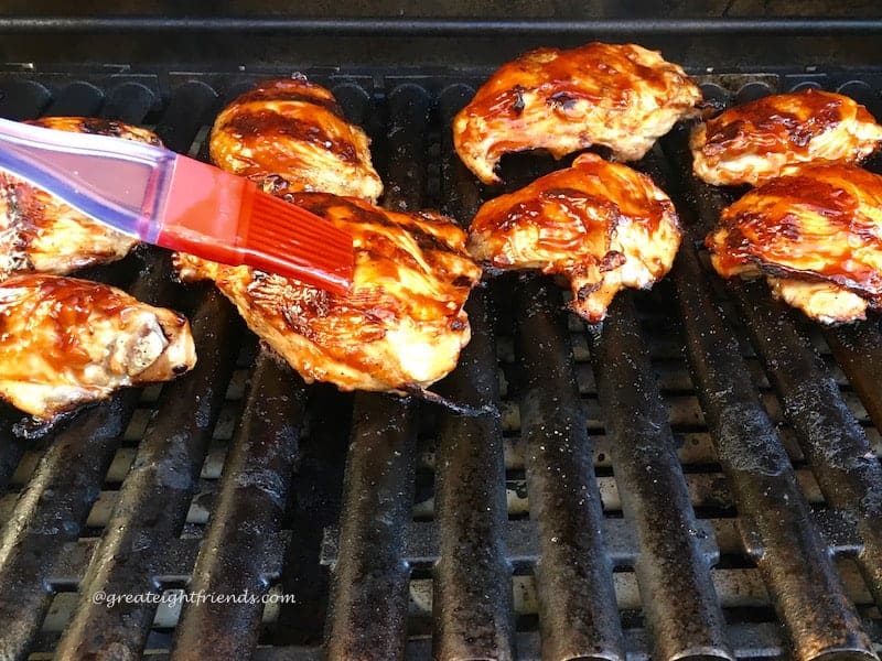 Chicken on a grill being brushed with barbecue sauce.