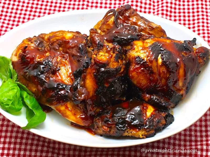 A white plate piled with barbecued chicken, garnished with a green leaf and sitting on a red and white checked tablecloth.