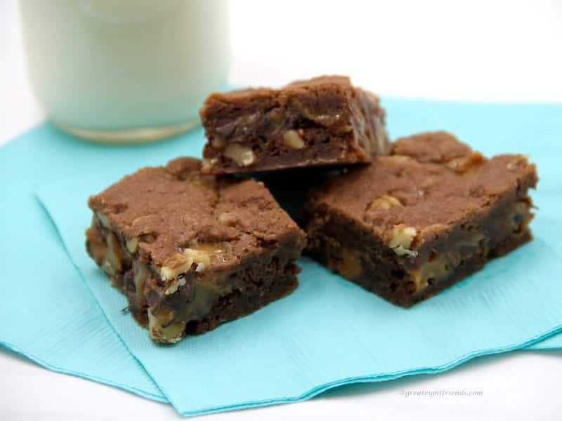 Three brownies sitting on a blue napkin with a glass of milk in the background.