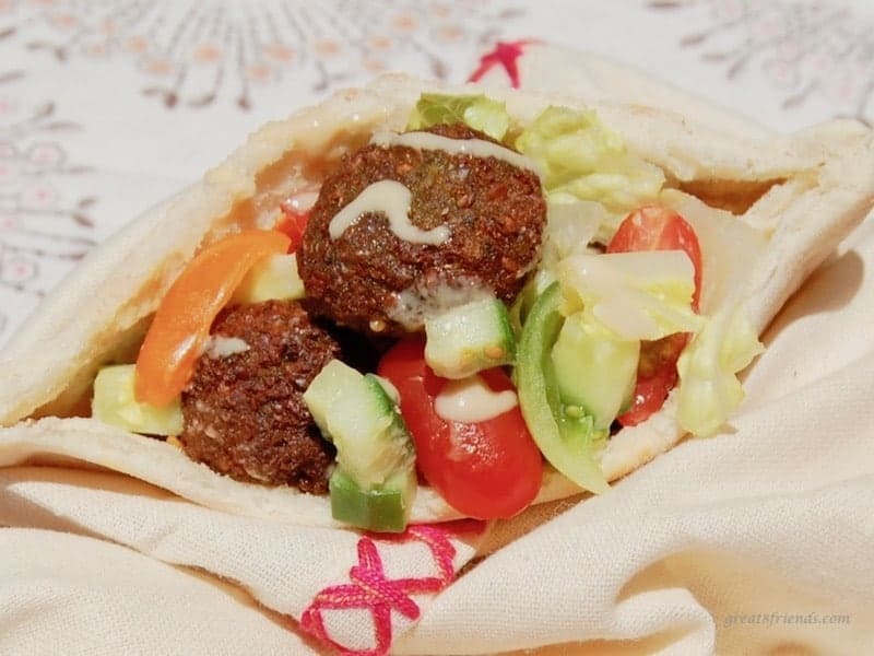An unclose view of falafels stuffed in a pita bread with chopped fresh cucumbers and tomatoes and tahini.