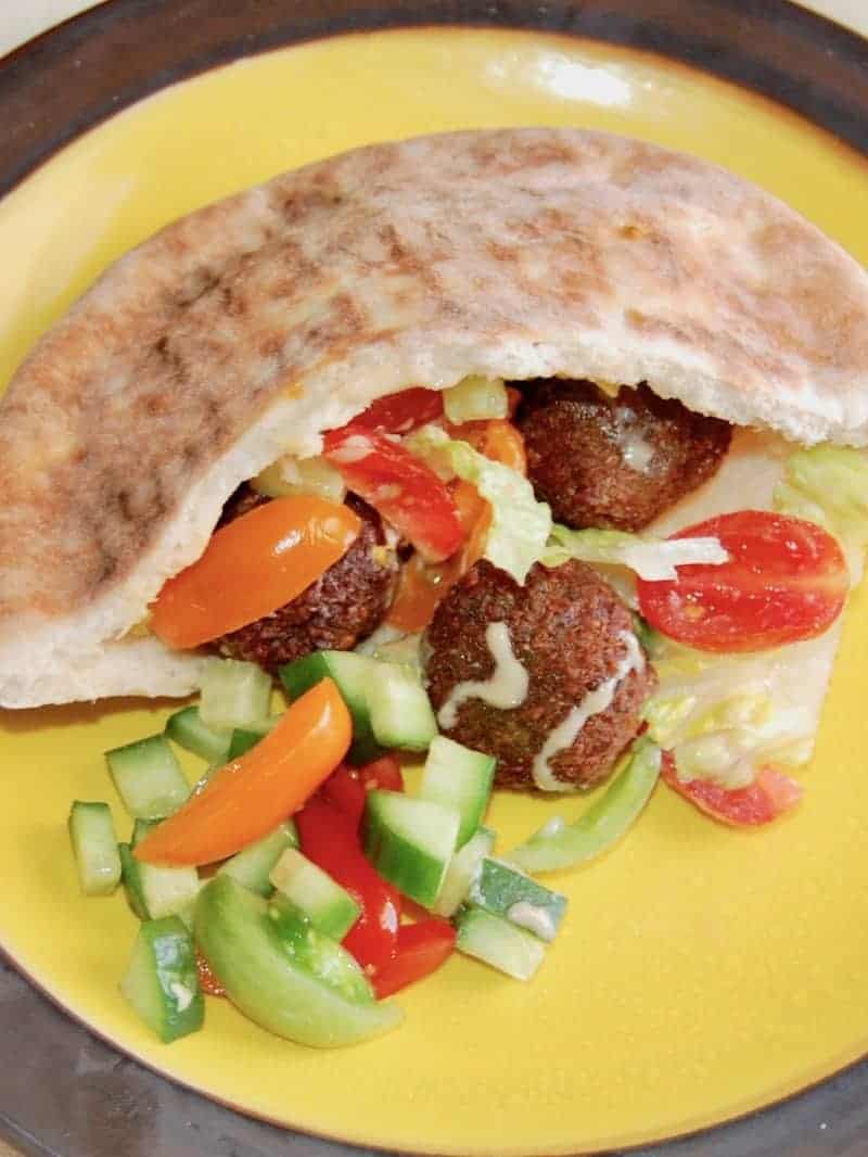 A Falafel served in a pita on a yellow plate with chop fresh vegetables.