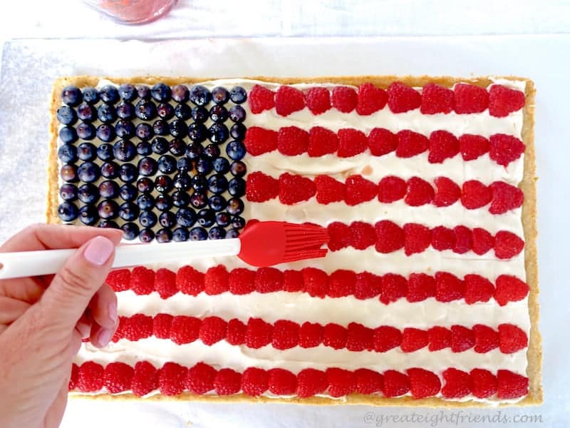 A hand brush syrup over the berries on an American flag fruit pizza.