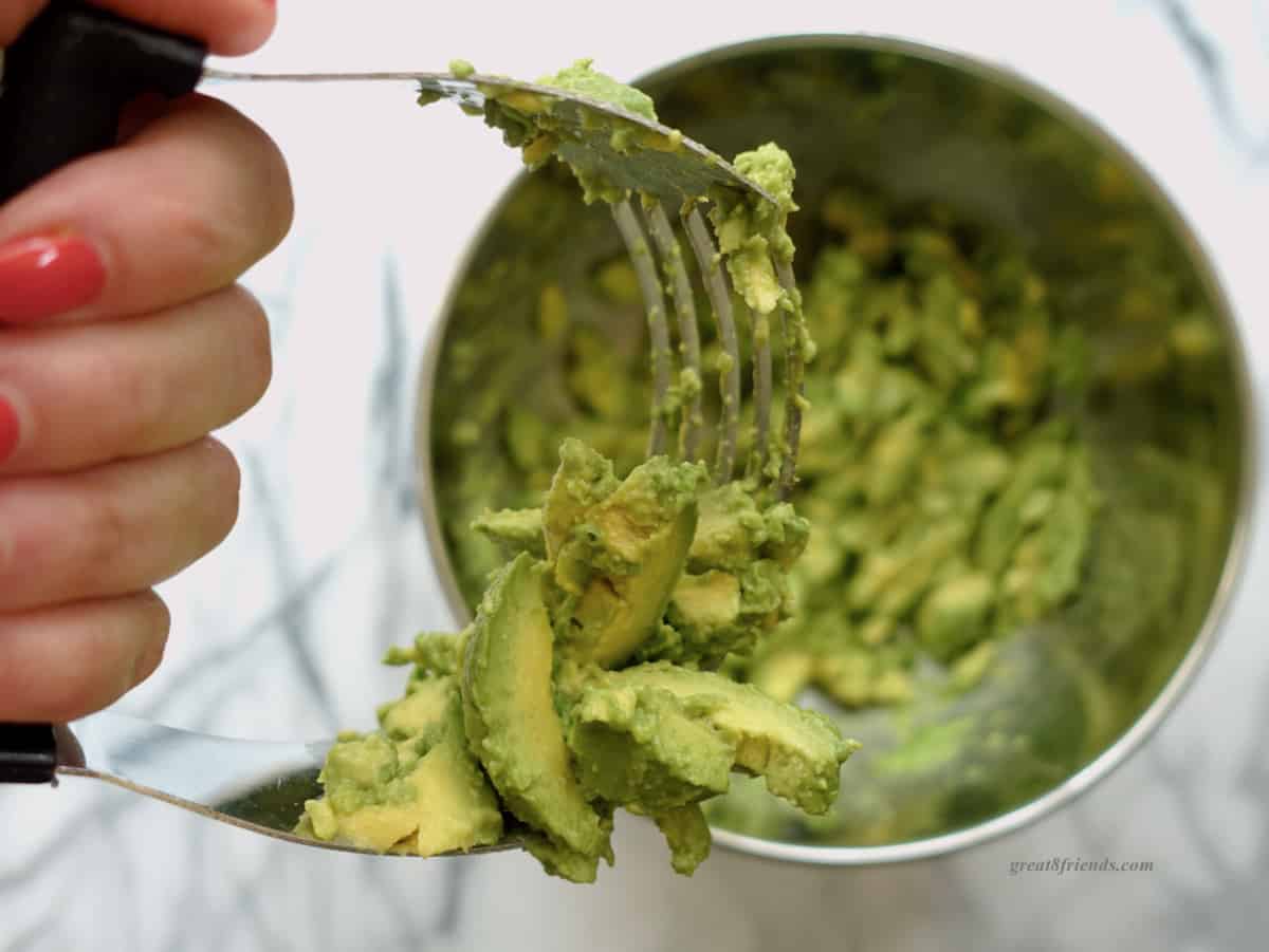 A hand holding a pastry cutter mashing avocados.