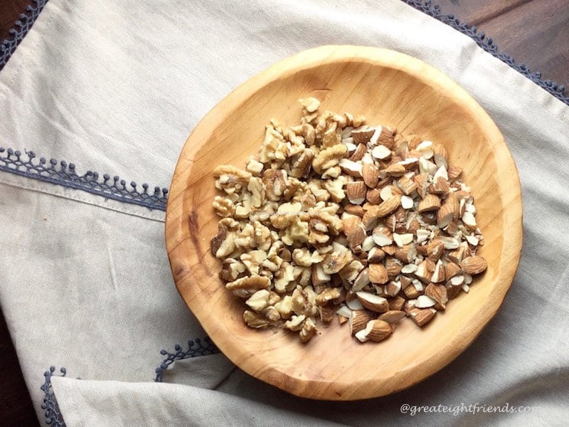 Wooden bowl of chopped almonds and walnuts on a white kitchen towel.