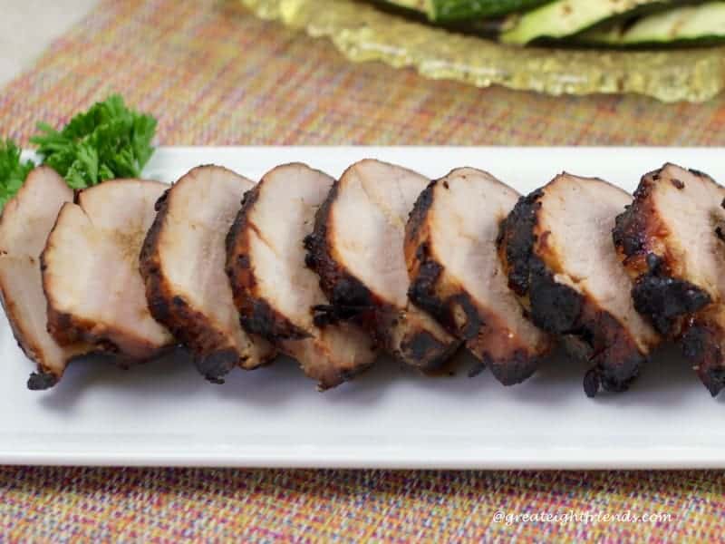 Side view of a sliced pork tenderloin with a parsley garnish.