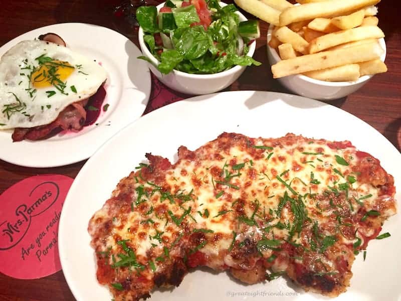 A white plate with chicken parma surrounded by fries and salad.