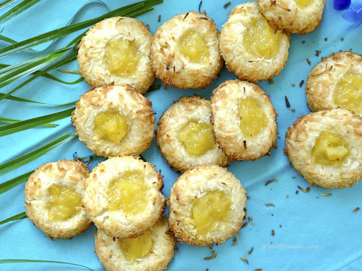 Overhead shot of coconut pineapple cookies laying on a blue background with a palm frond in the corner.