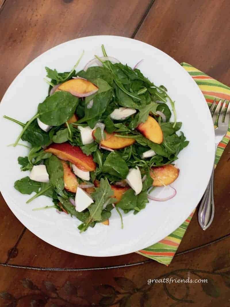 Overhead shot of green salad tossed with nectarines and burrata cheese. A fork is alongside the white salad plate. 