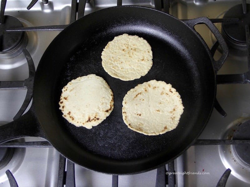 Three small corn tortillas in a black cast iron skillet on the stovetop.