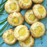 Over head close up shot of coconut pineapple thumbprint cookies on a blue background.