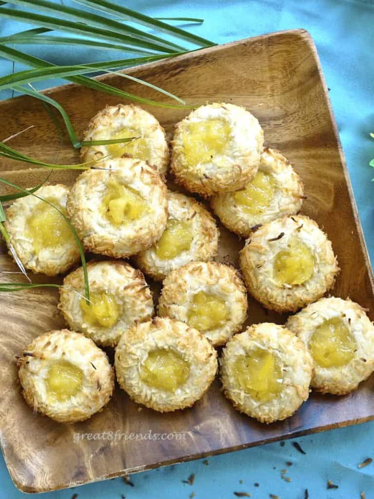 Over head shot of coconut pineapple thumbprint cookies on a square wooden platter on a blue background.