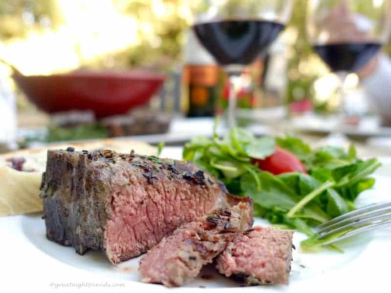 A sliced lamb chop on a plate with a glass of wine in the background.