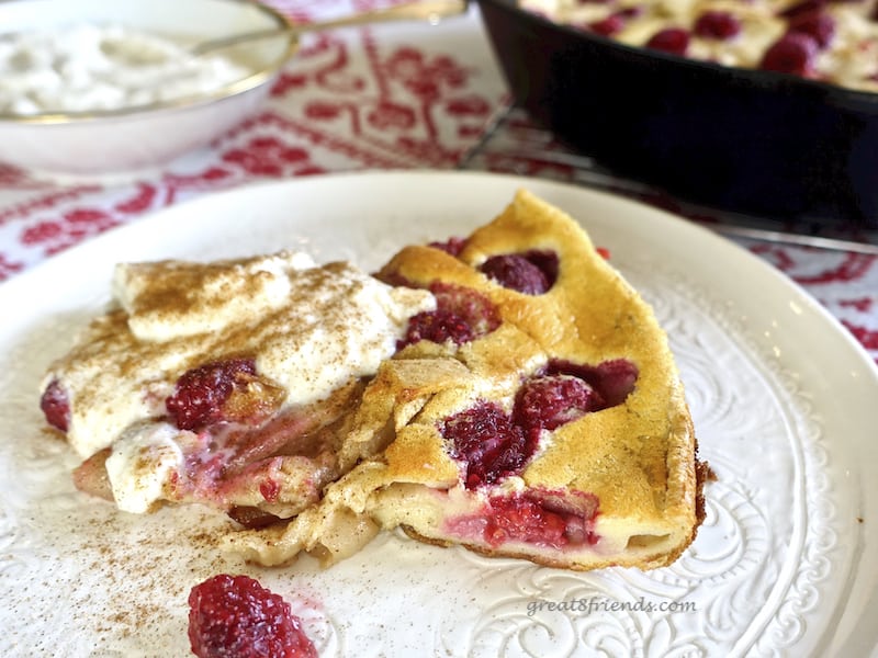 A slice of Apple Berry Dutch Baby on a white plate with a dollop of ricotta cream and cinnamon on top.