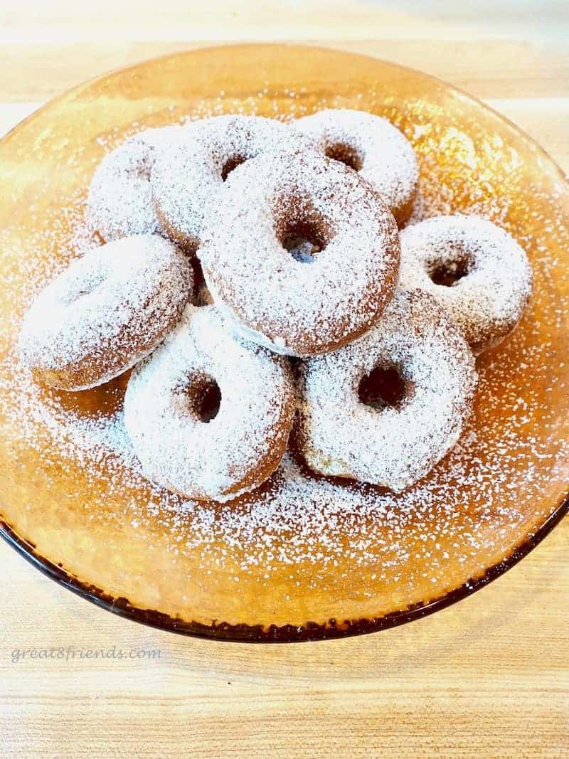 Overhead shot of a pile of donuts, covered with powdered sugar on an orange glass plate.