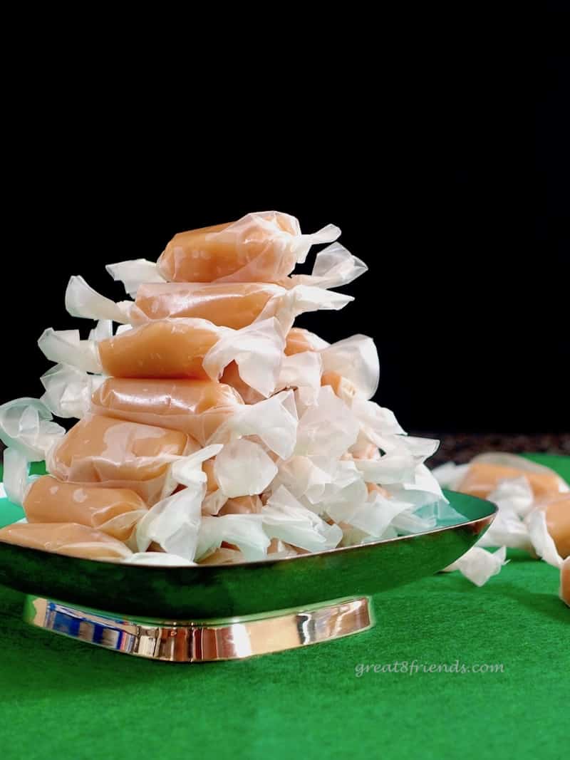 Homemade caramel candy wrapped in waxed paper and stacked on a metal dish.