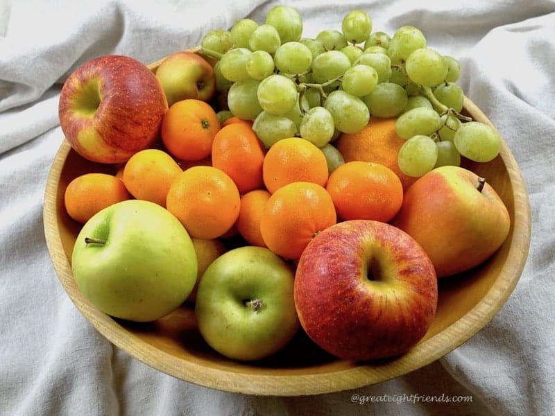 wooden bowl full of fresh apples, grapes, and tangerines.