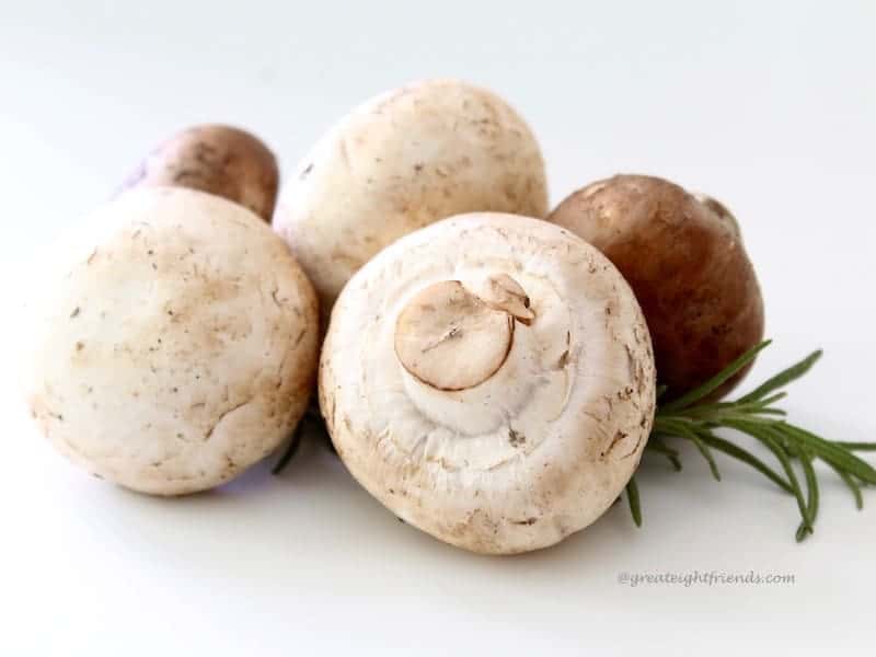 Upclose photo of five fresh raw mushrooms with a sprig of rosemary.