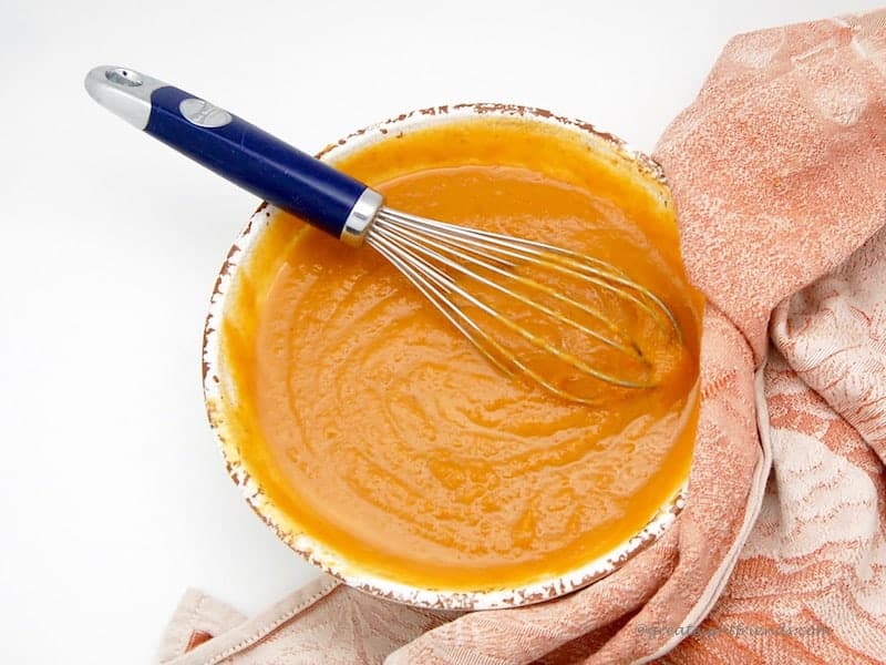 A bowl of orange batter with a whisk.