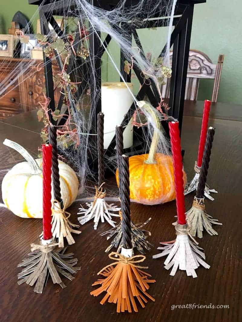 Eight Sweet Witch's Brooms made from candy vines and paper standing in front of some pumpkins and a candle.
