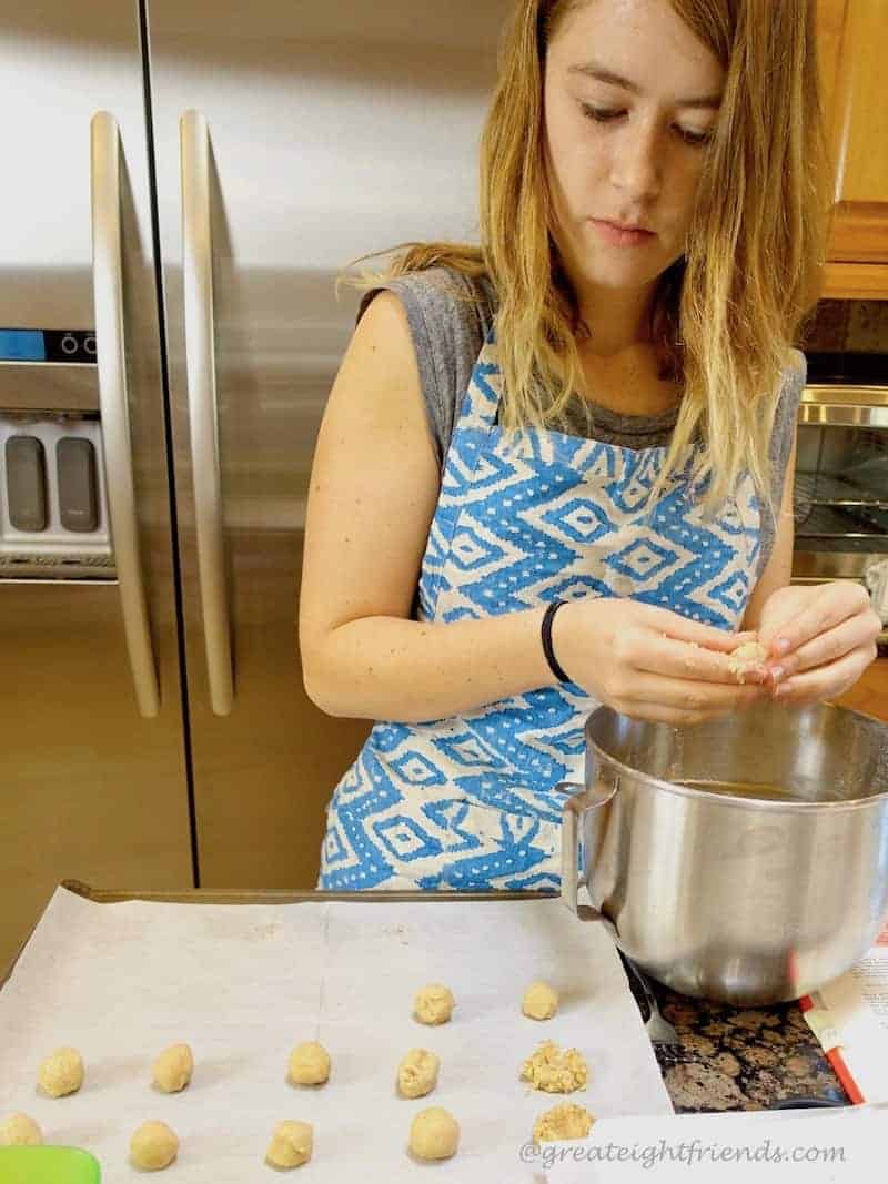 A young woman rolling raw dough into balls.