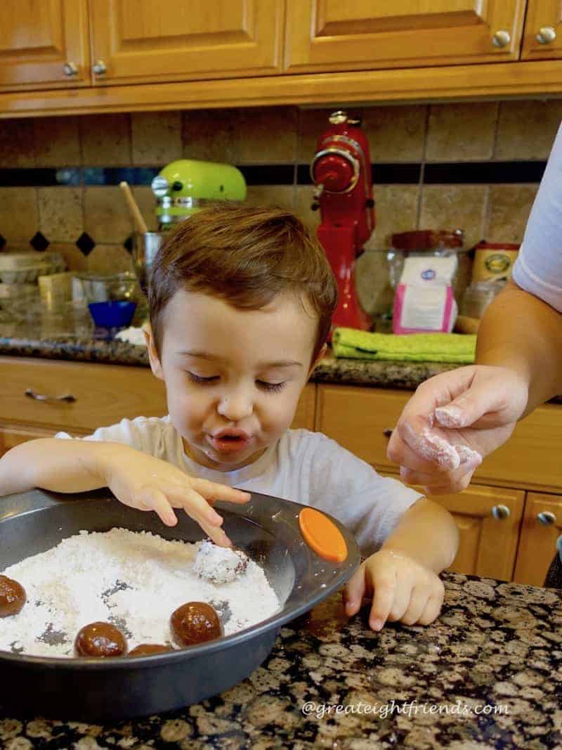 A little boy rolling cookies in powdered sugar.