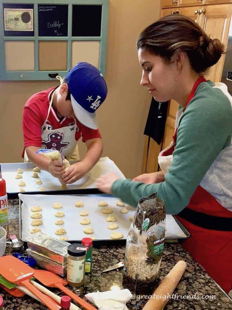 Two people piping cooking dough onto baking sheets.