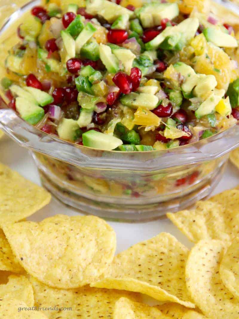 Unclose photo of pomegranate avocado salsa in a glass bowl with tortilla chips scattered around the bowl.