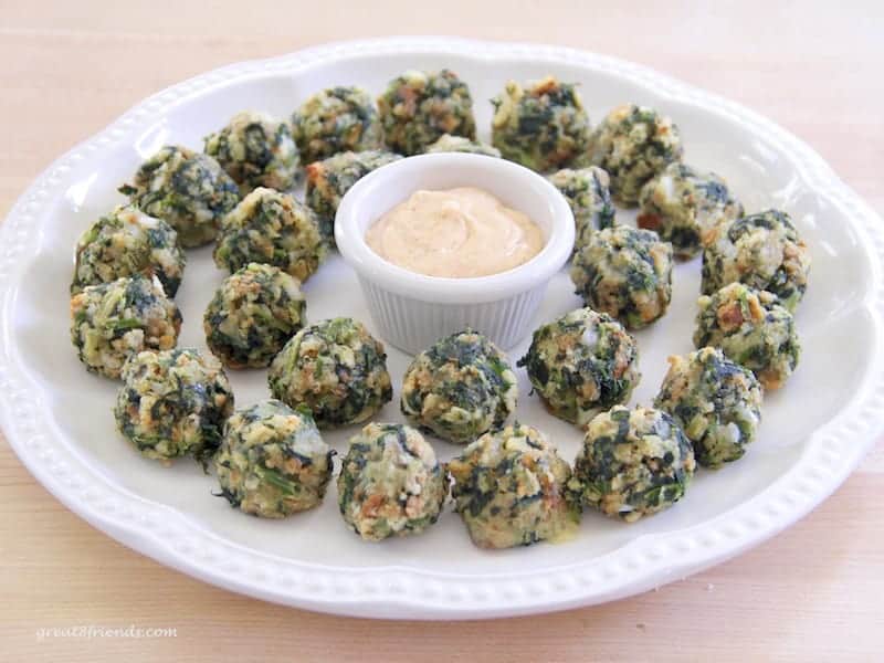 Spinach balls on a round white platter with a small bowl of dip in the center.