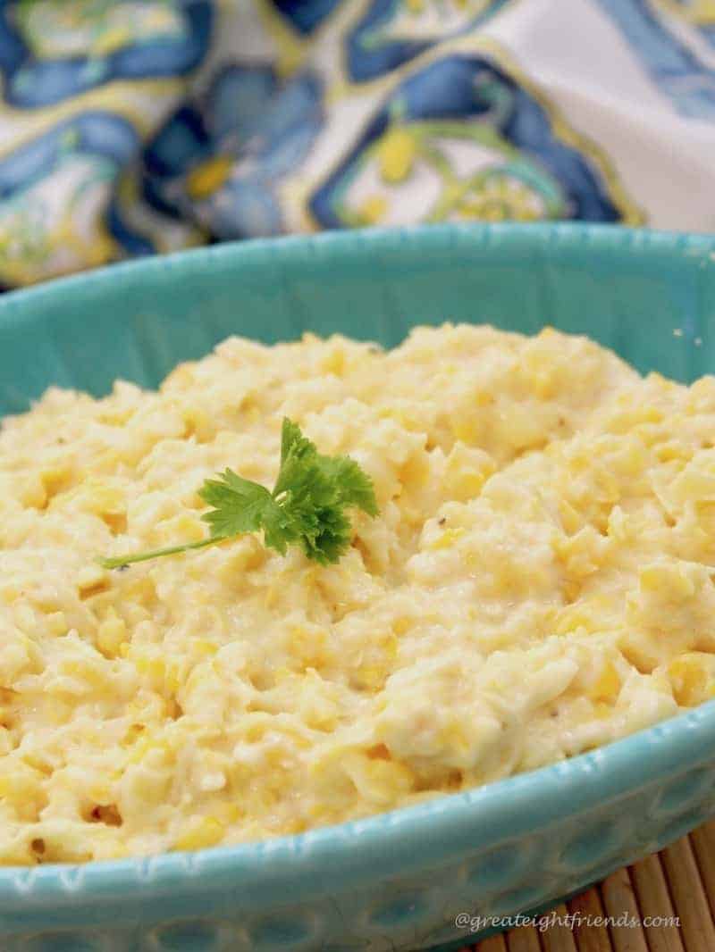 A close up of a blue bowl filled with creamed corn with a parsley sprig on top.