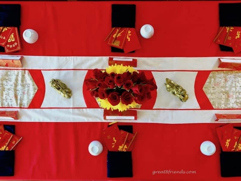 Overhead shot of a table set for Chinese New Year with a red tablecloth, Asian style runner and rose centerpiece.