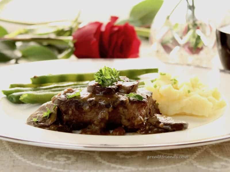 A plate of steak, mashed potatoes and a green vegetable with a red rose in the background.