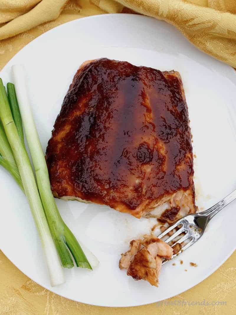 Overhead photo of glazed salmon on a white plate with a green onion.