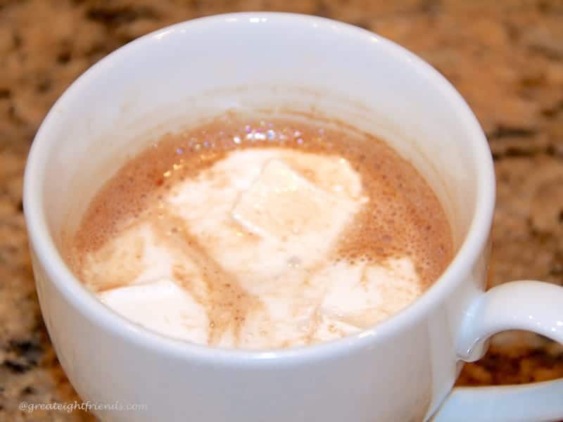 Hot chocolate with melted marshmallows on top in a white mug.