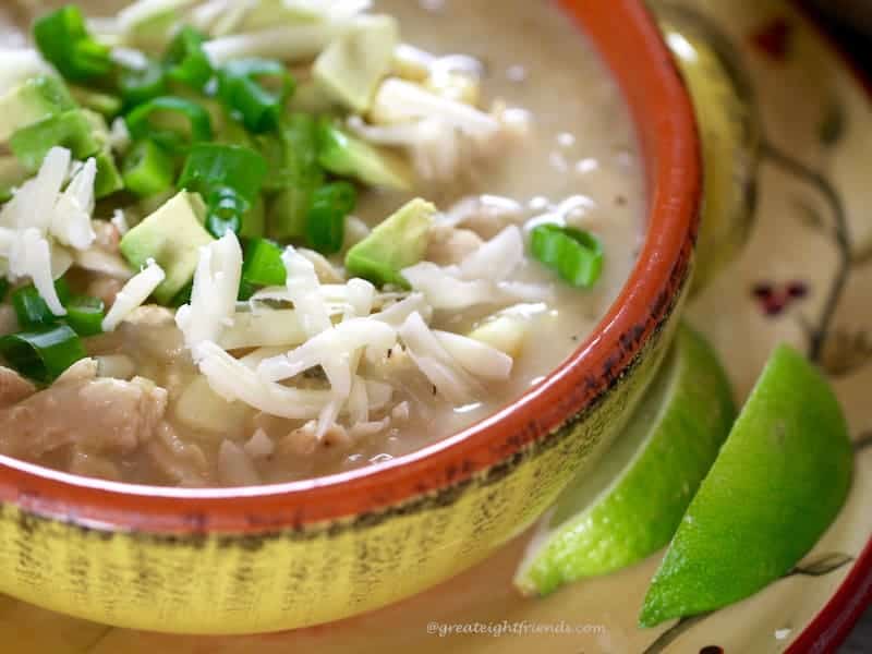 White Cheddar Chicken Chili in a yellow and orange bowl toped with cheese and avocado with sliced lime on the side.