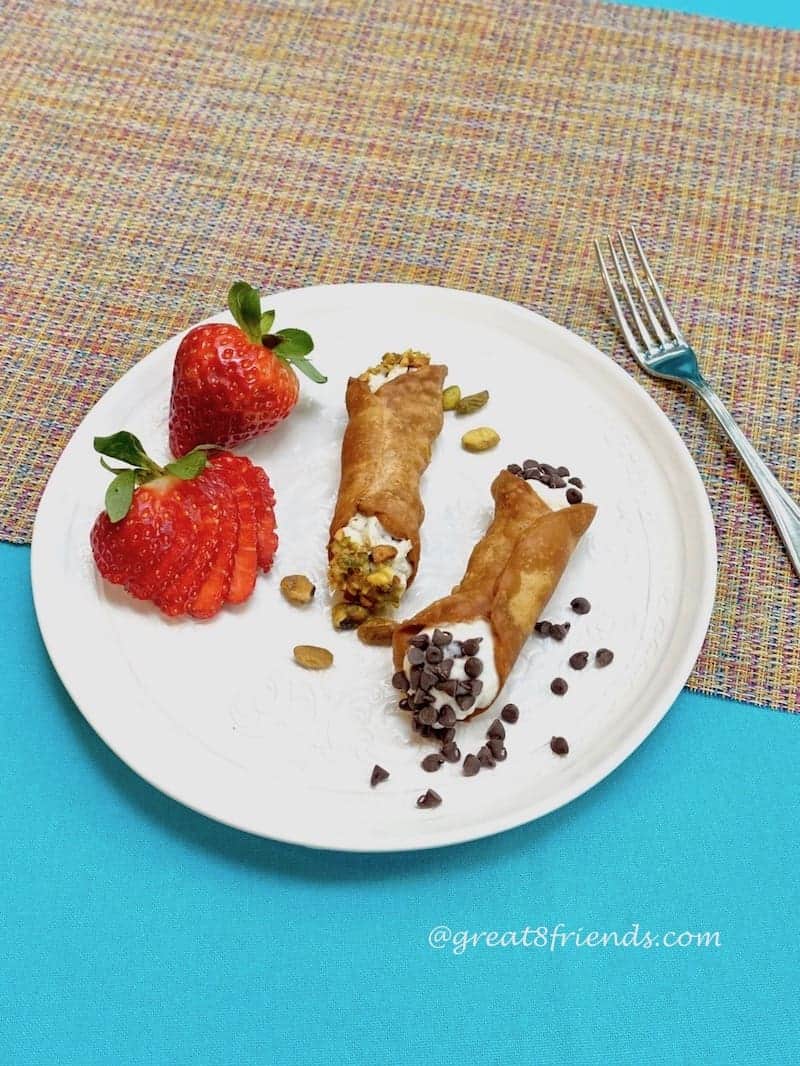 2 cannoli on a round plate with 2 strawberries.