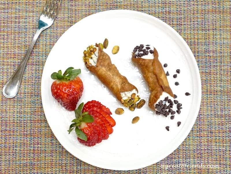 Overhead shot of 2 filled creamy crispy cannoli and 2 strawberries.
